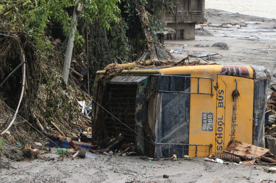 A yellow school bus fell beside ravaged trees. Nepali writing and the bus number are visible on the vehicle.