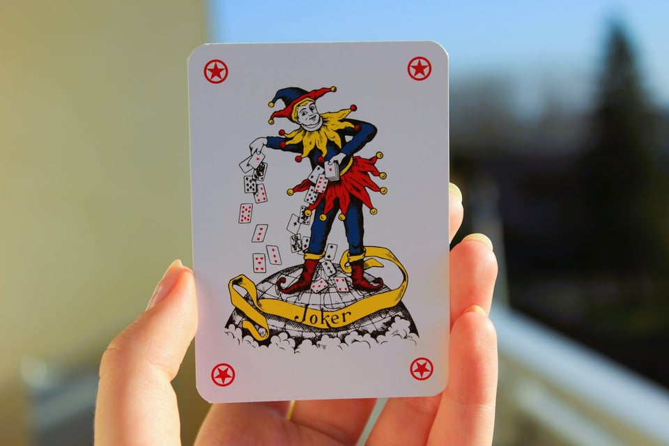 A hand holding up a joker card. Photo by Kateryna Kamenieva on Unsplash.
