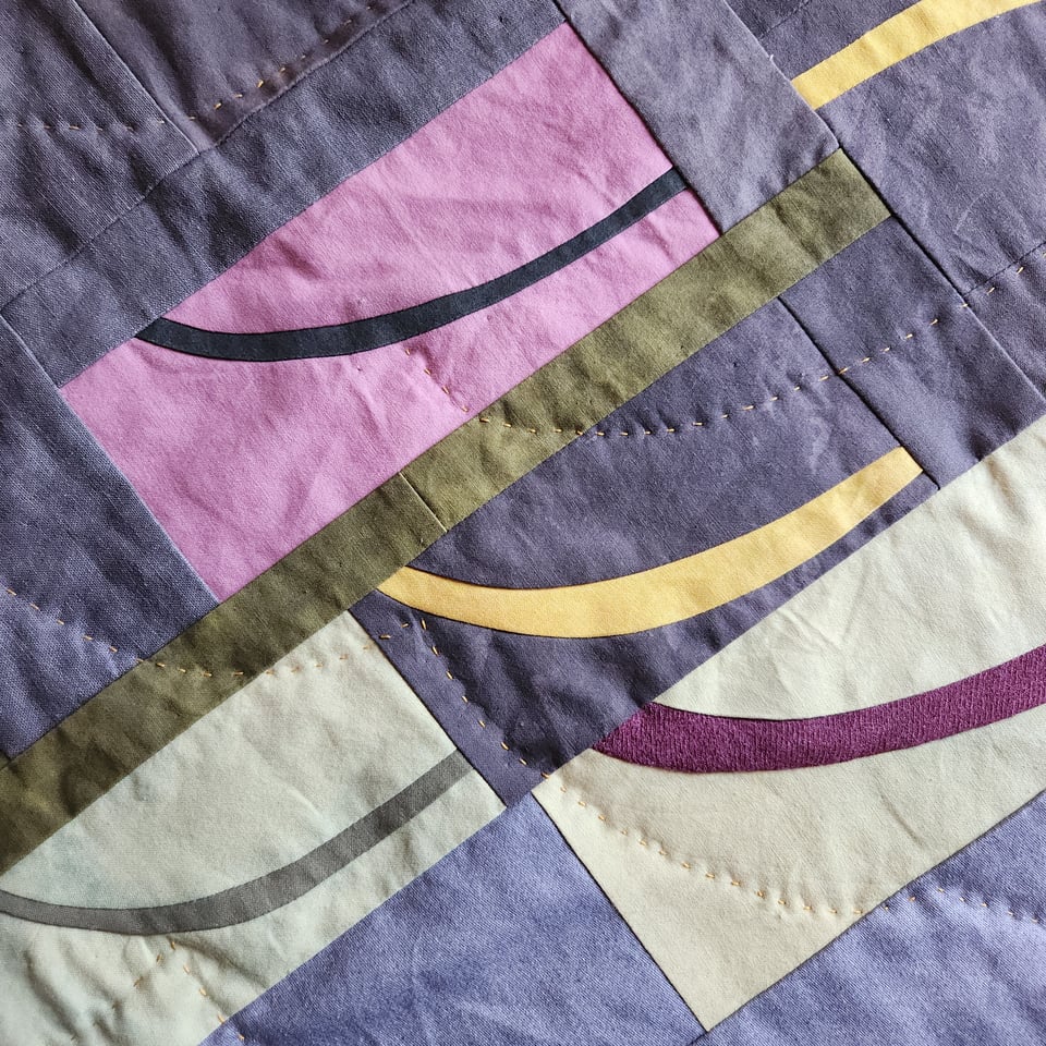 Close up photo of Arabesque 2 in progress, a patchwork quilt by Sarah Atlee, with fabrics in gray, pink, yellow green, and olive green. Sarah’s hand stitches are visible.