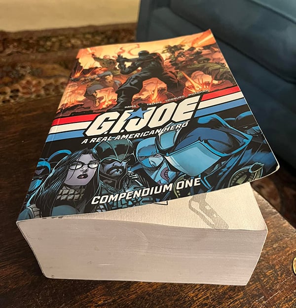 A giant, fat book with the title G Joe Compendium sitting on a table. Various characters like Cobra Commander and the Baroness and Snake Eyes are on the cover.