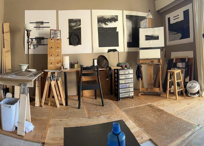 A studio space with wood flooring, sawhorse tables and art hanging on the walls.