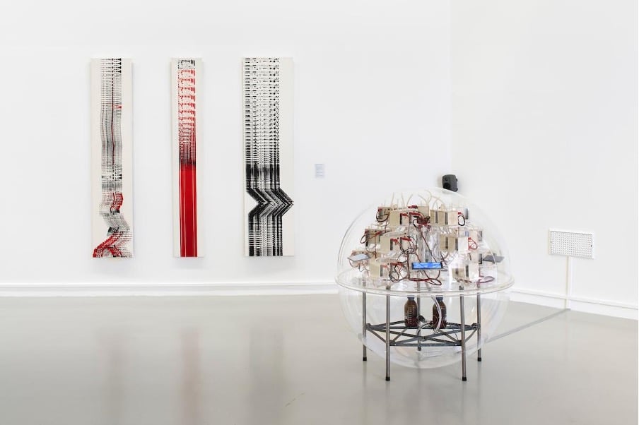 a clear spherical ball sculpture in an art gallery, with three images on the wall