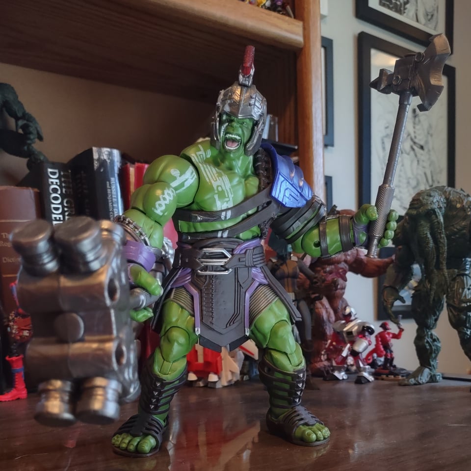 A huge (well eight or nine inches tall) action figure of the Hulk stands on a wooden desk. He's wearing futuristic gladiator armor and holding a gigantic hammer in one hand an an axe in the other.