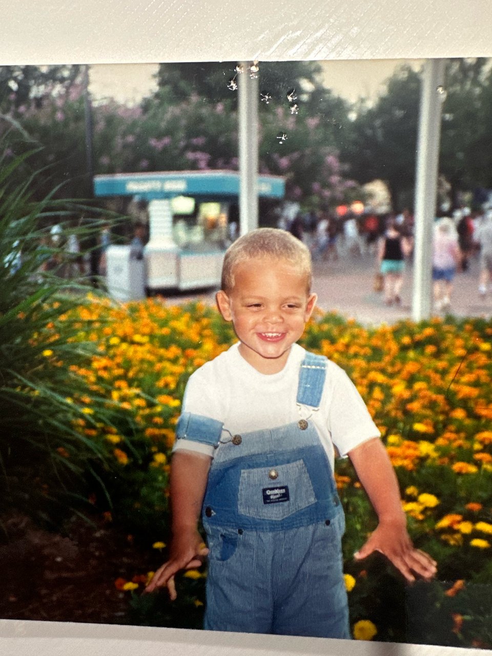 a printed photo of me as a toddler, wearing osh kosh b'gosh overalls in front of a sea of flowers.