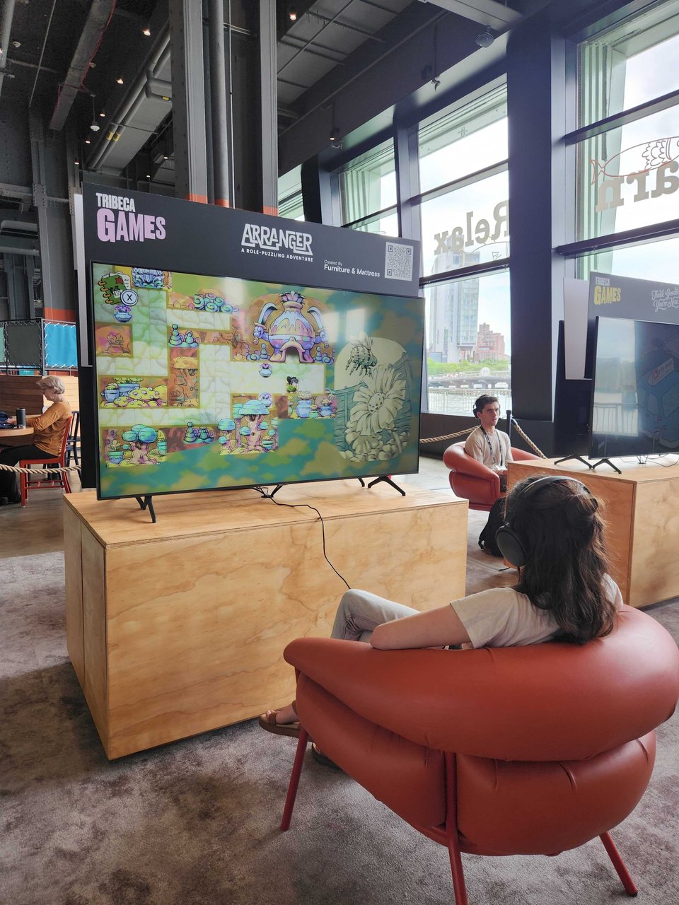 A spacious room at Pier 57 in NYC, in which someone is playing Arranger on a big TV