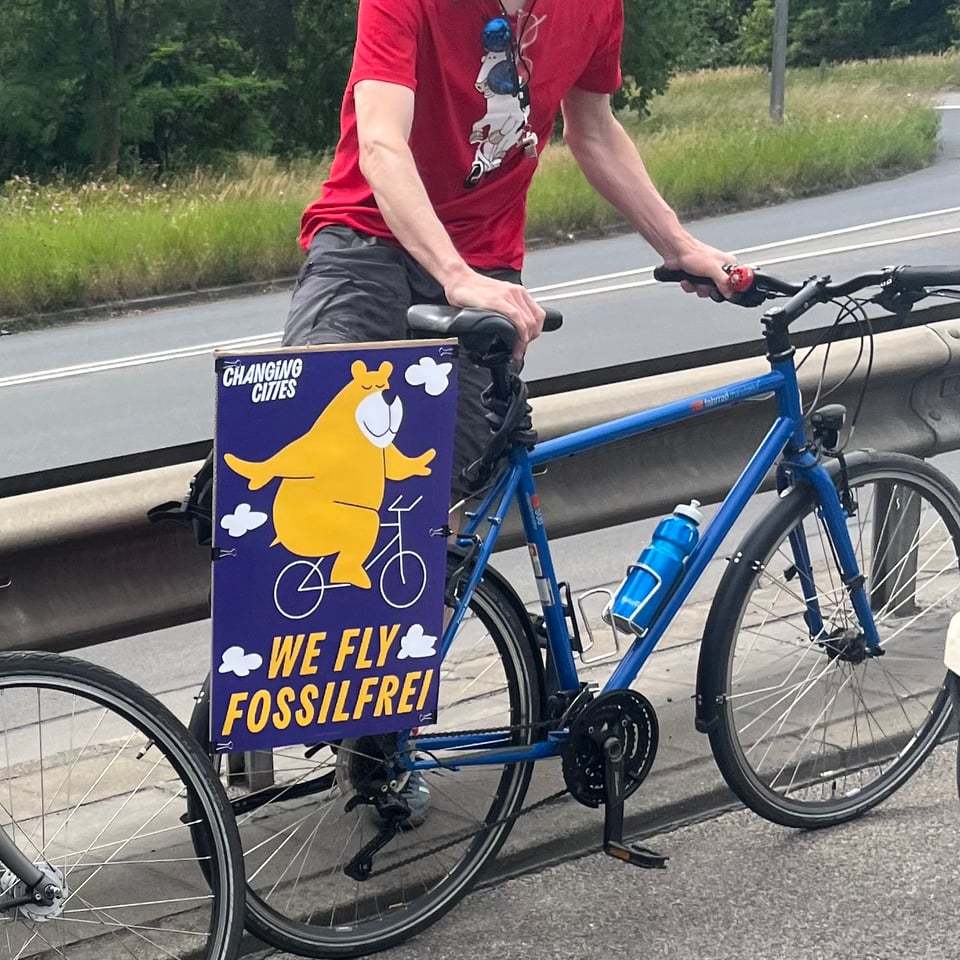 A bike with the poster "We fly fossilfrei" and a cartoon of a bear with outstretched arms riding a bike.