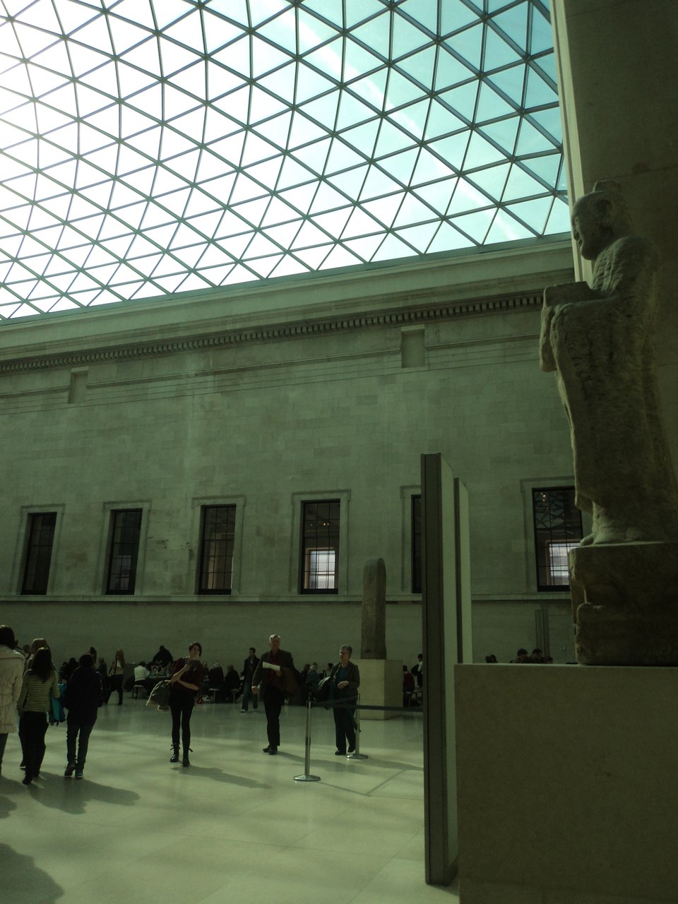 a view from inside the modern British Museum rotunda, with glass dome and people wandering about the floor.