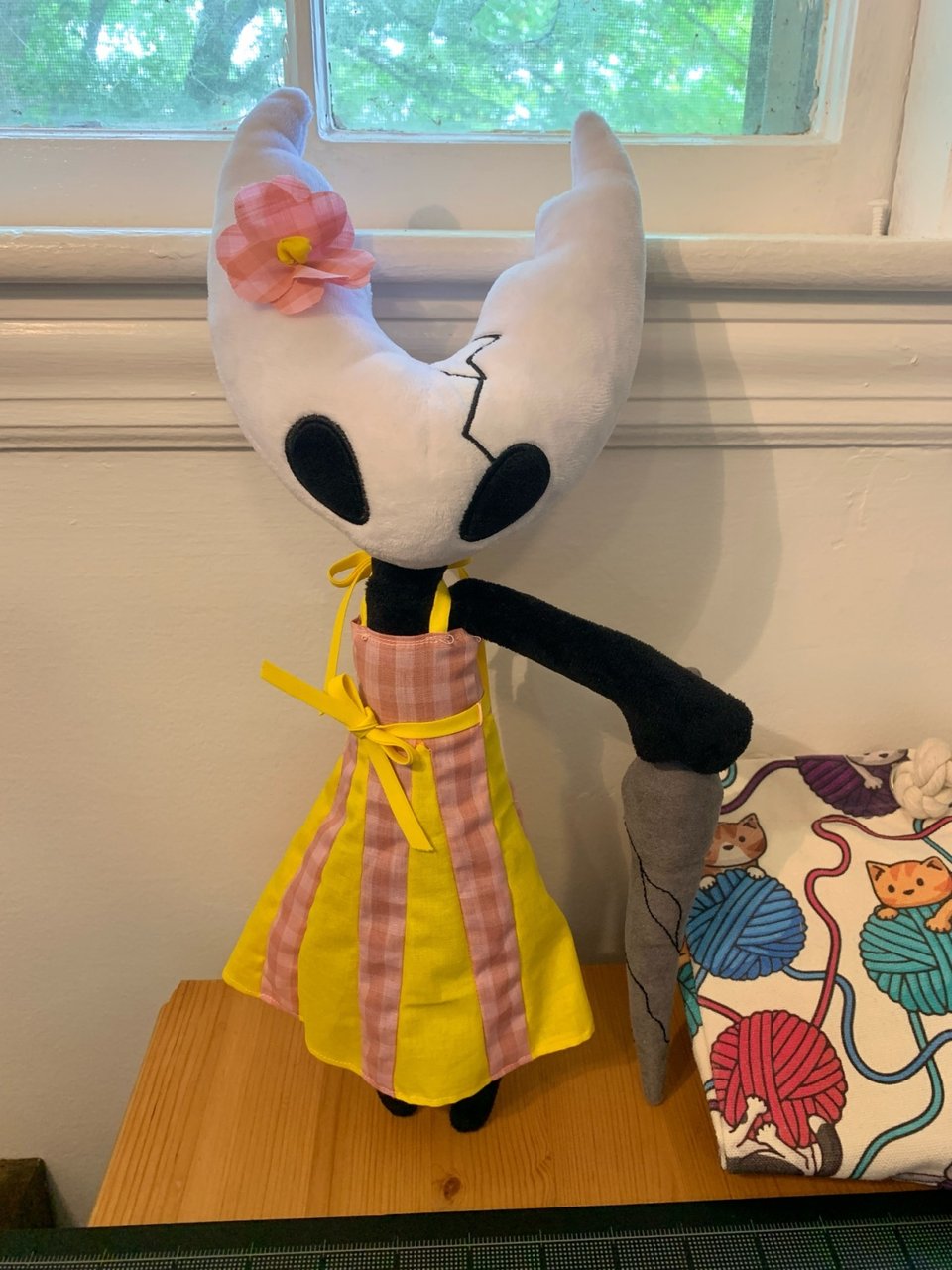 a hollow knight plushie wearing a homemade pink and yellow sundress.