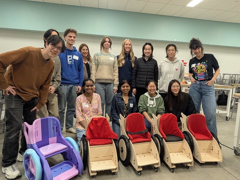 12 Berkeley students and Dana posing with the four new toddler mobility trainers and a 3D printed example chair