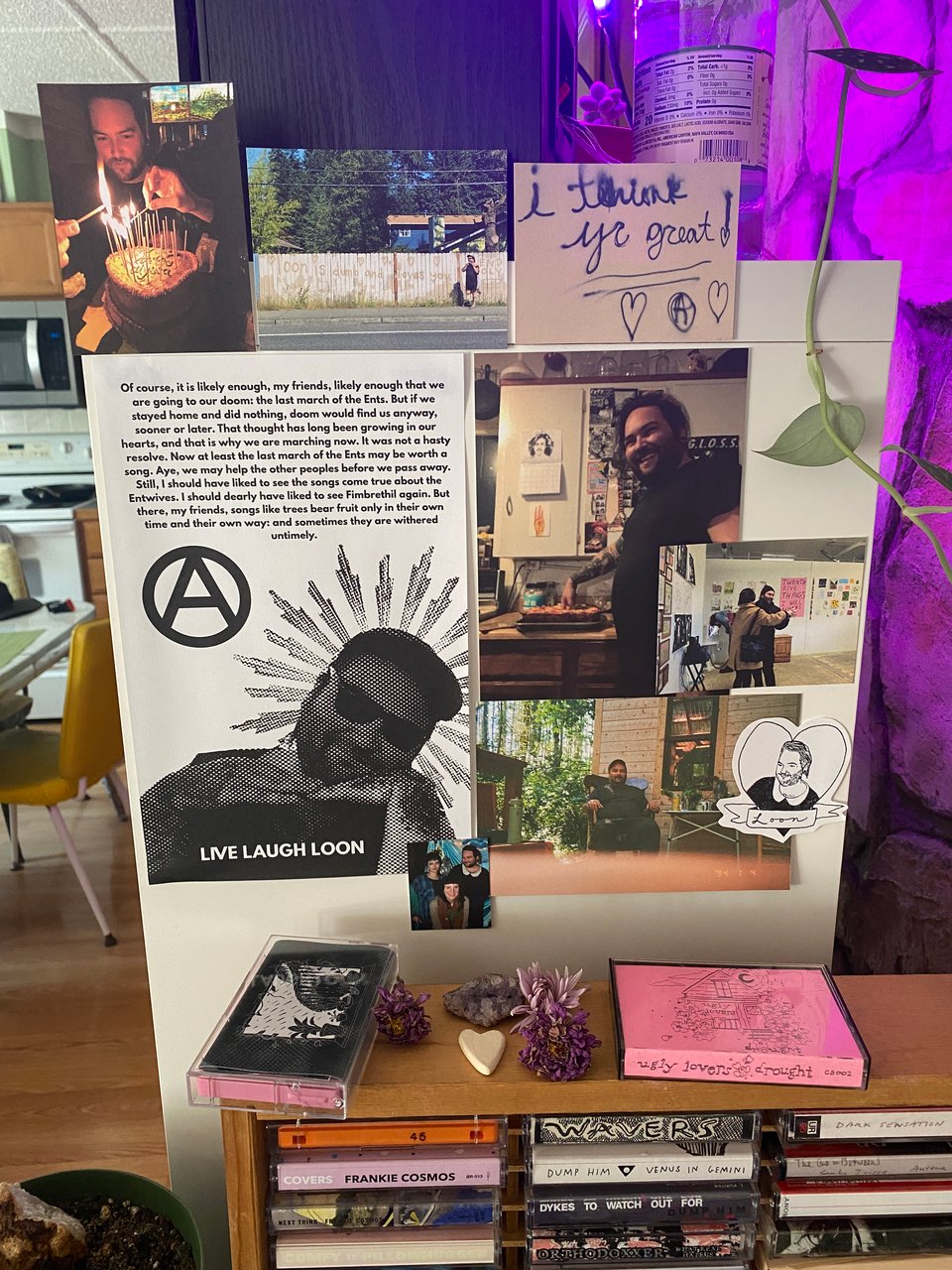 an alter for loon, lots of photos taped up above some cassette tapes and dried flowers.