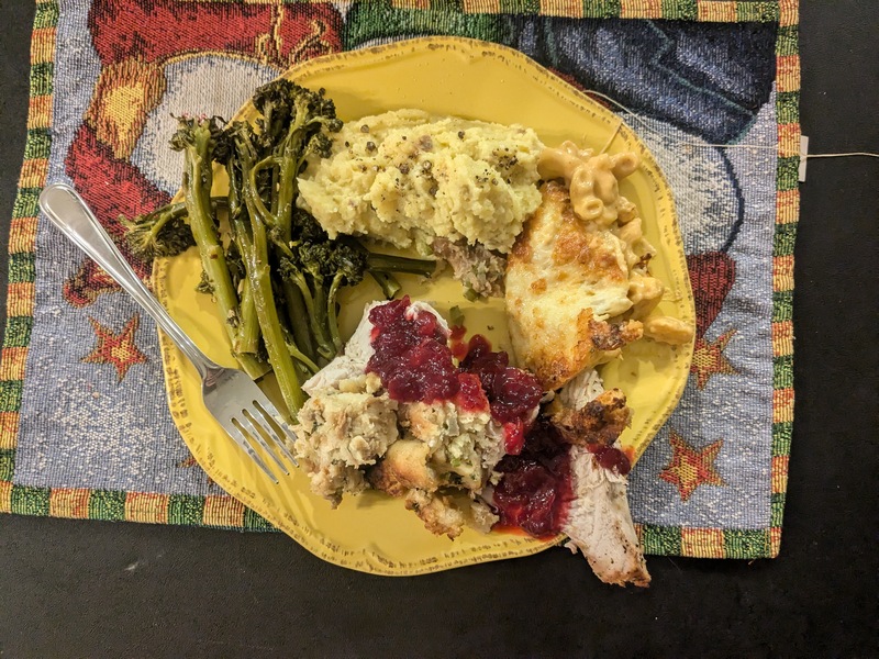 A plate of food: baby broccoli, mashed potatoes, macaroni and cheese, and turkey with stuffing topped with cranberry sauce.