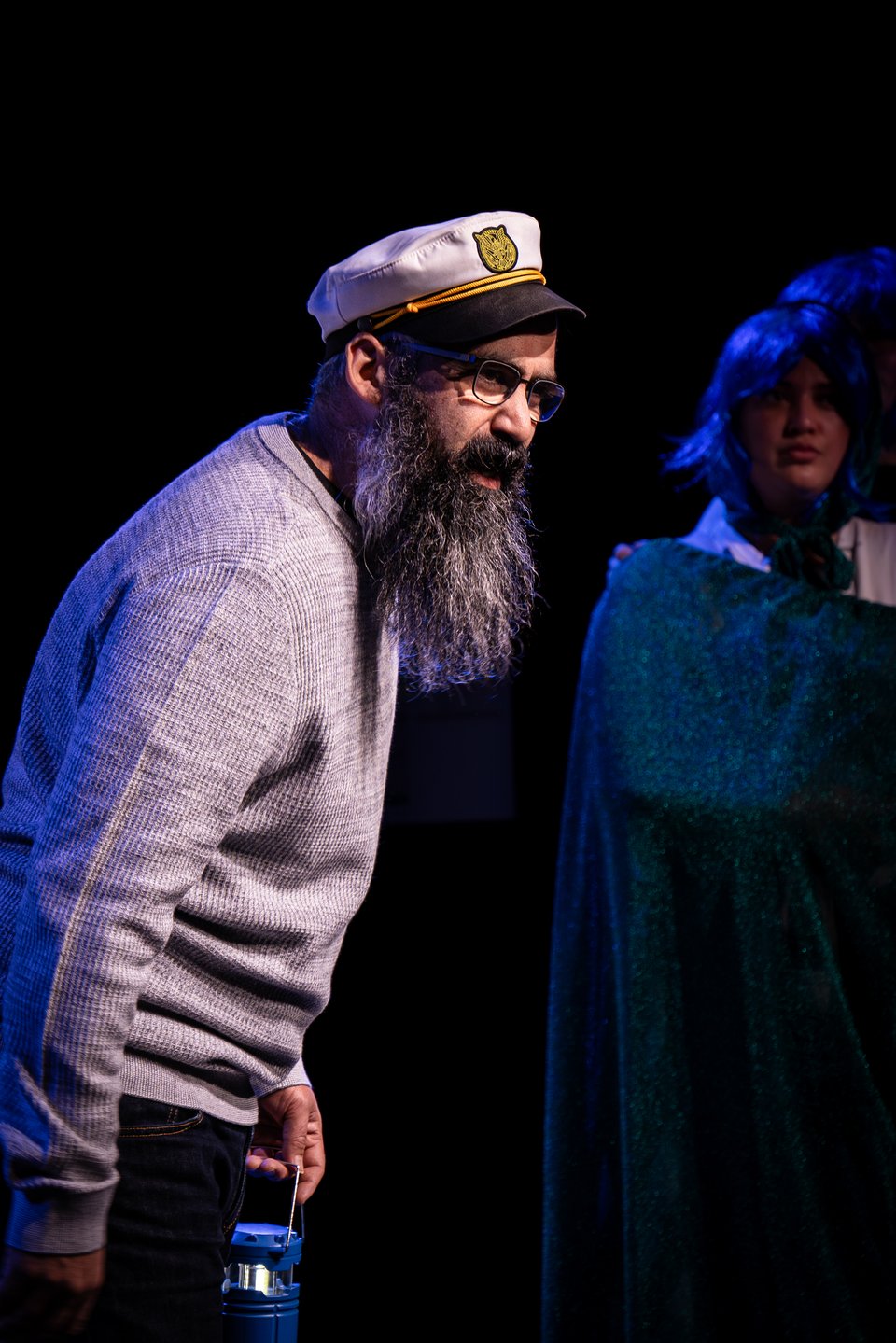 Jerome in sea captain uniform regaling the crowd while Mo, in shadows, watches in the background