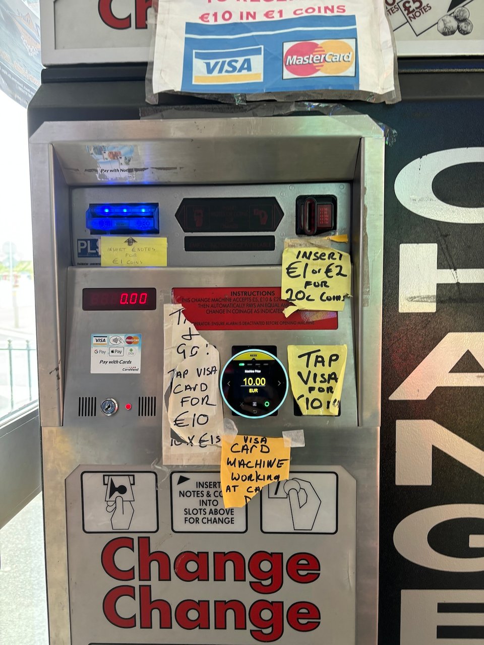A change machine in an arcade with five separate ragged bits of paper stuck on it with instructions about how to get change