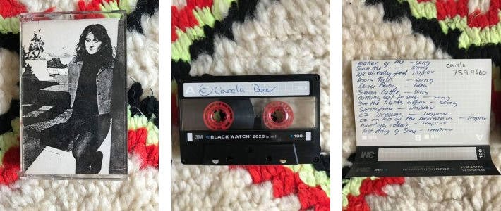 Three pictures of the Carola Baer cassette tape. The first one shows for dressed in a light jacket, blacks letter, dark stirred and black tights; she's in the foreground while in the background there is a statue garden with a large statue of a man on horseback. The second photo is of the cassette; it is black and has only on it written in handwriting her name,