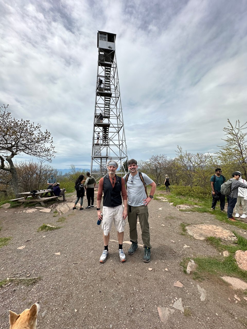 Photo of two white male hikers in front of a fire tower on an overcast day