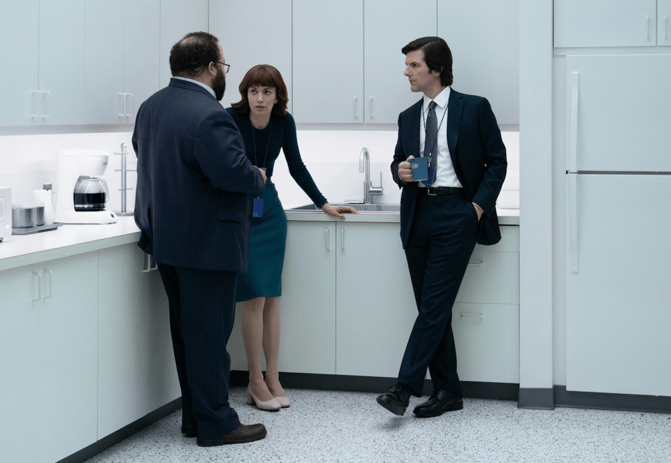 The Lumon Industries gang, in the all-white kitchen of their office, having a confab. Michael Scott's character looks especially "office-y" with his ID on a lanyard around his neck and a coffee mug casually in his hand.