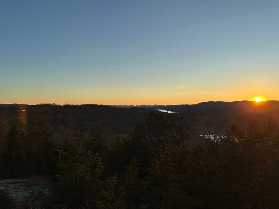 photo of woods, hills, and reservoir in late afternoon, with sun setting on the right side
