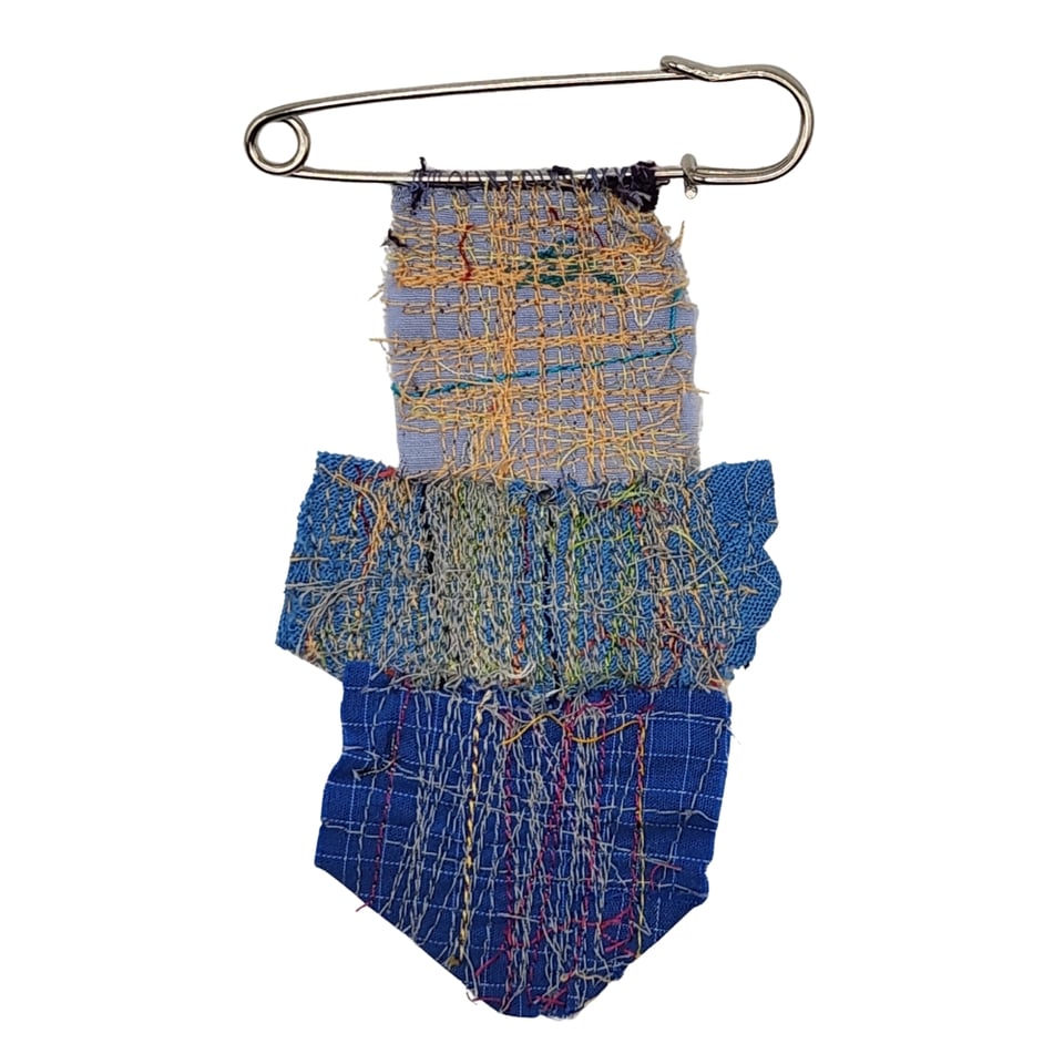 Photo of a brooch made of fabric scraps attached to an oversized safety pin.