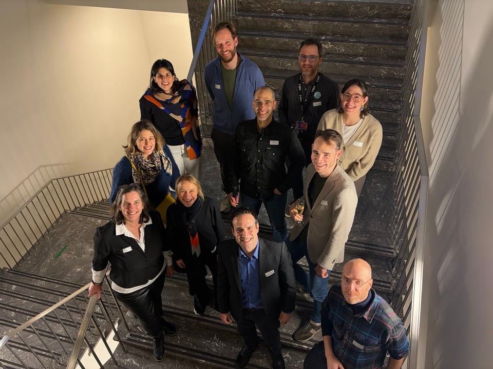 11 people stand in a stairwell all smiling up at the camera.