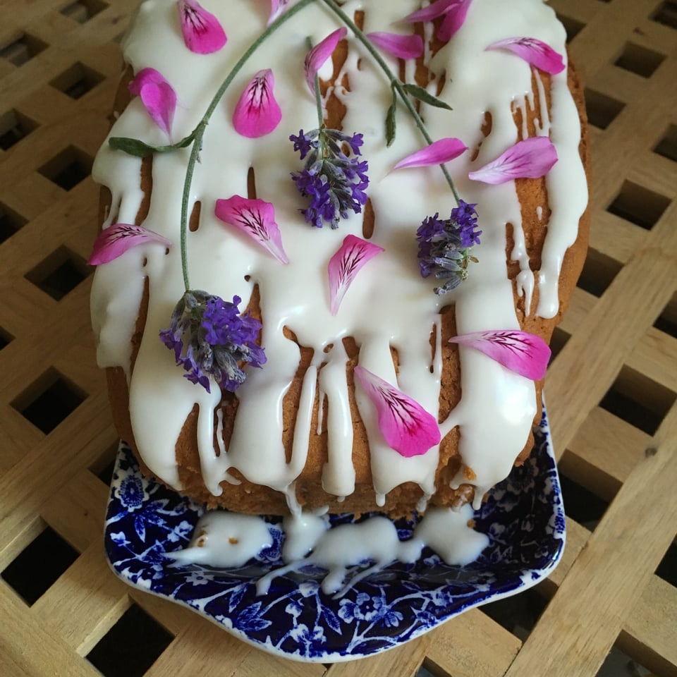 A loaf cake iced and decorated with sprigs of purple lavender and bright pink pelargonium petals. Image by Rowan Ambrose