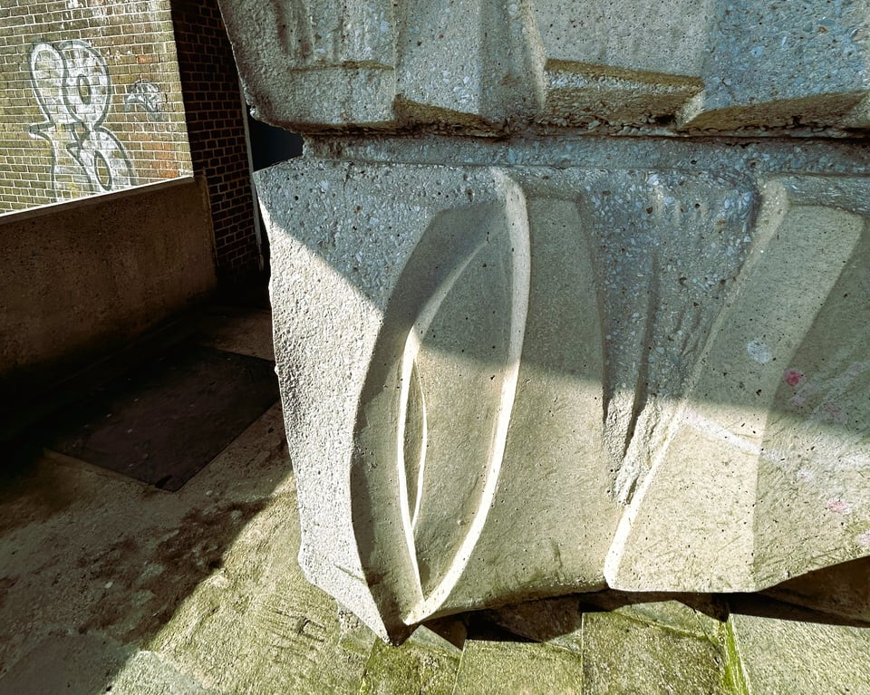 A cast concrete block that is part of the central column of a staircase. It is pale cream, and has been shaped to form a bas relief of organic curves. Some parts have been polished smooth on purpose. The steps and rest of the stairwell is grotty.