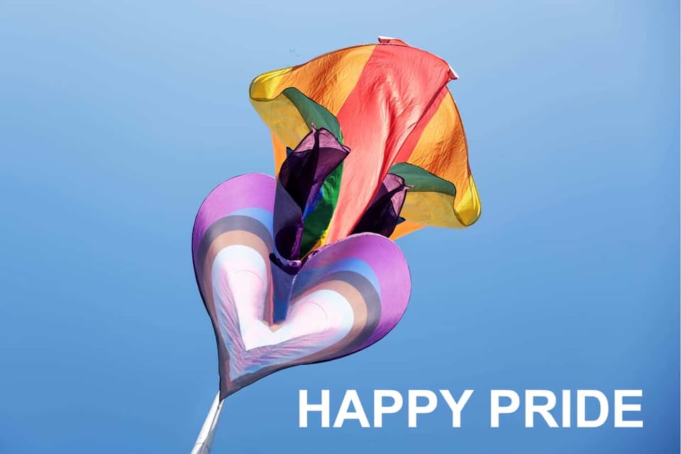 A photo of a heart shaped pride flag in the sky