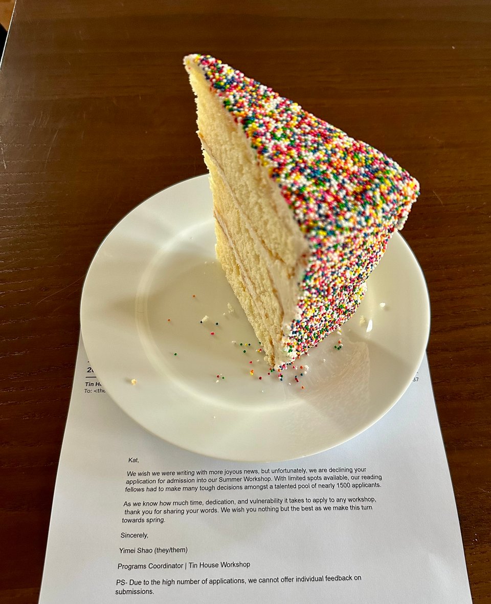 A very tall piece of white layer cake covered in sprinkles on a plate on top of a letter telling the writer their summer writing workshop application has been declined.