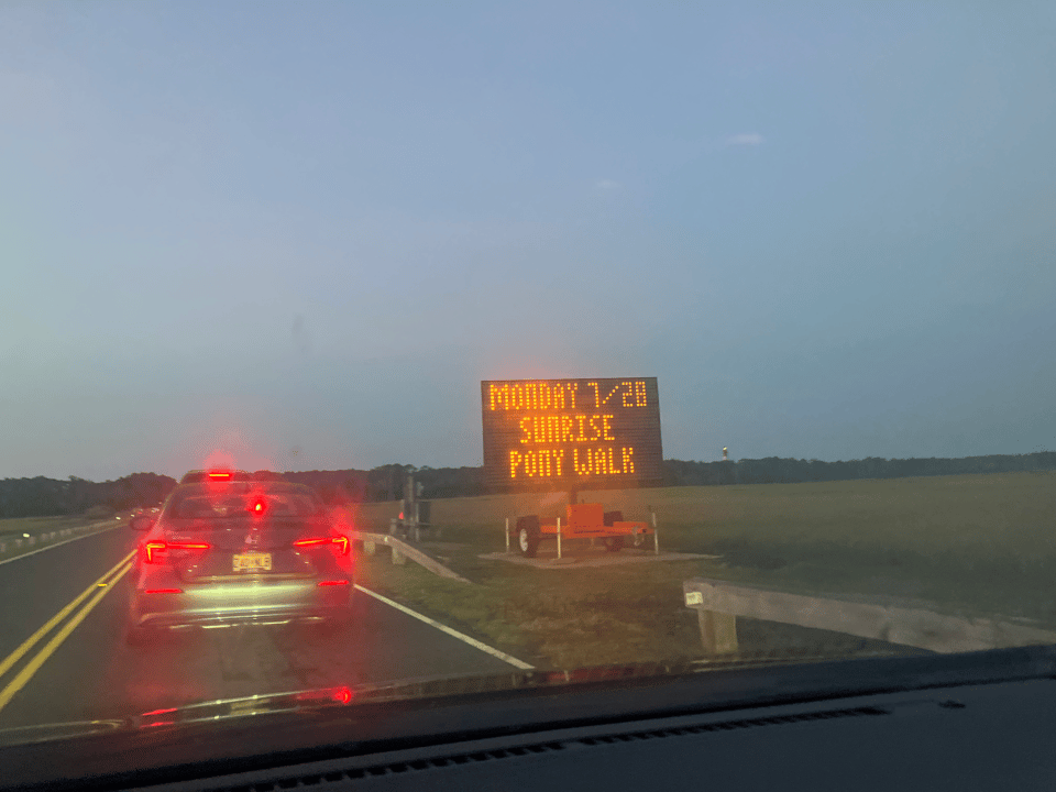Traffic stalled on the causeway. A marquee reads “Monday 7/28 Sunrise Pony Walk.”