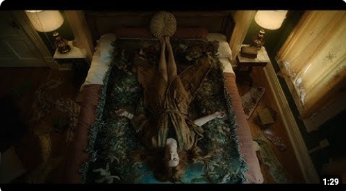 Screenshot of the YouTube thumbnail for the saint Clare film trailer. It shows a bird's eye view of a young woman laying on a bed, arms outstretched and red hair spread around her.