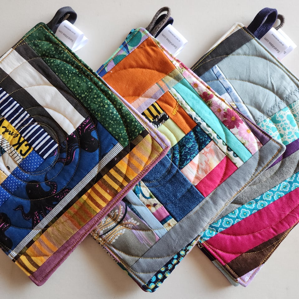 Photo of three sets of patchwork potholders made by Sarah Atlee. They include fabrics in all colors held together by a spiral pattern of stitches.