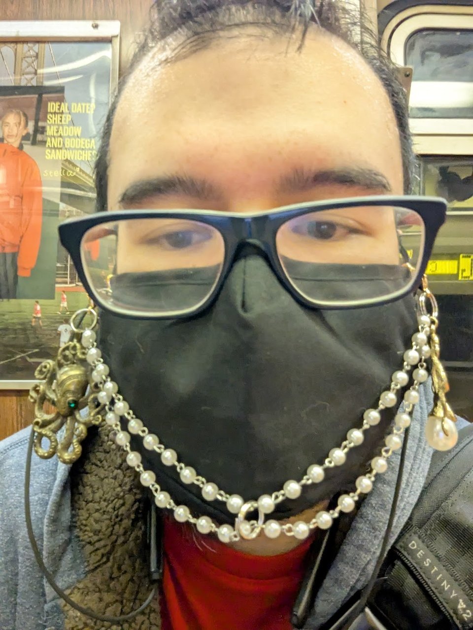 A tired Mikkel wearing glasses and a black face mask with a mask chain of pearls and two squid trinkets.