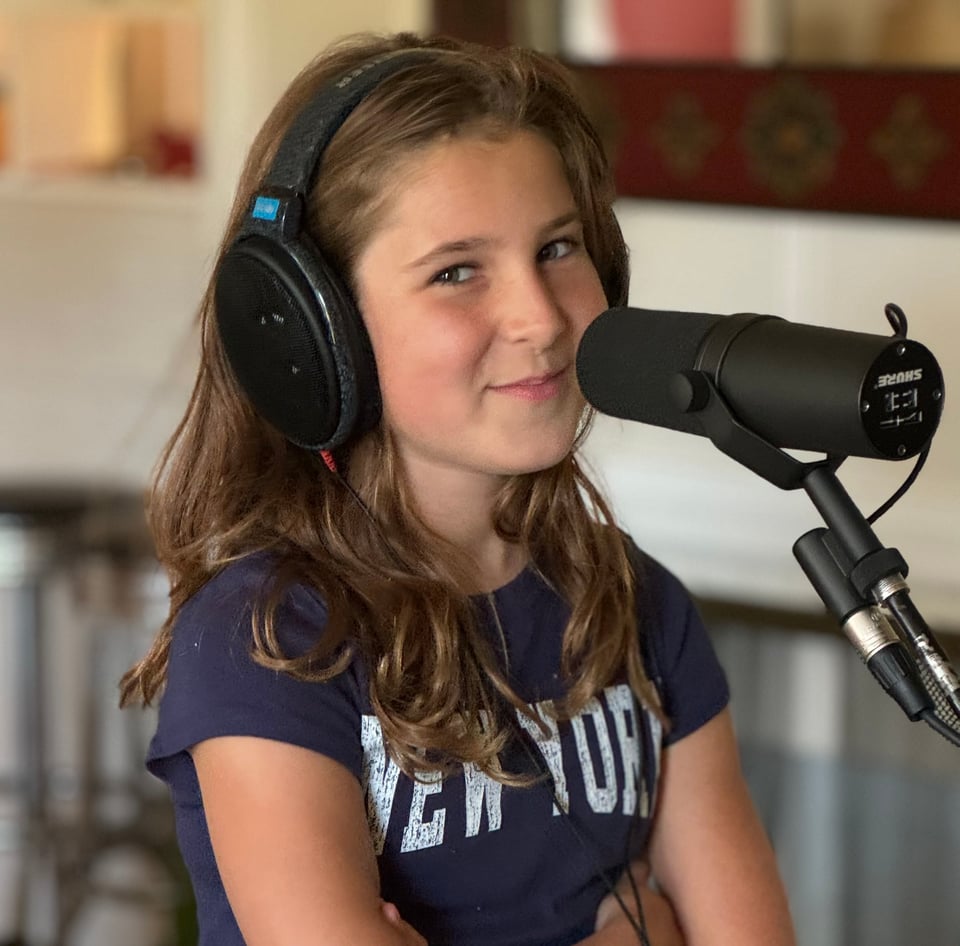 A 10-year-old girl in a shirt that reads "New York" sits in front of a microphone.