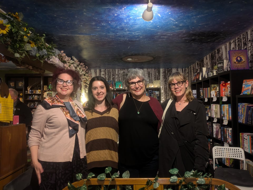 Four white women poets pose for a photo inside a magical bookstore called Felixology. Three of them have glasses, all of them are smiling.