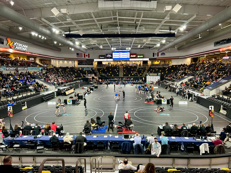 Photo of women's wrestling matches taking place on six mats across an arena.