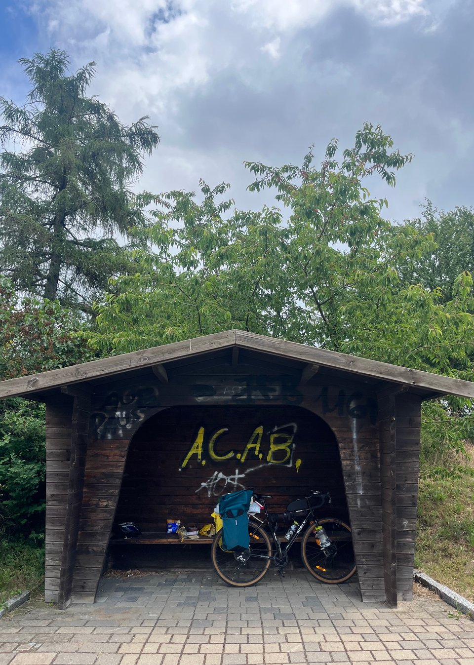 A wooden bike shelter with "A.C.A.B." spray painted on it, and a bicycle inside.