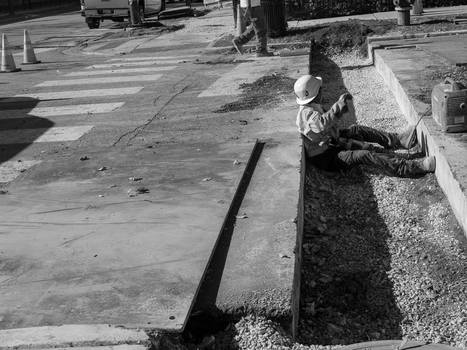 A construction worker sitting in a trough cut into the road.