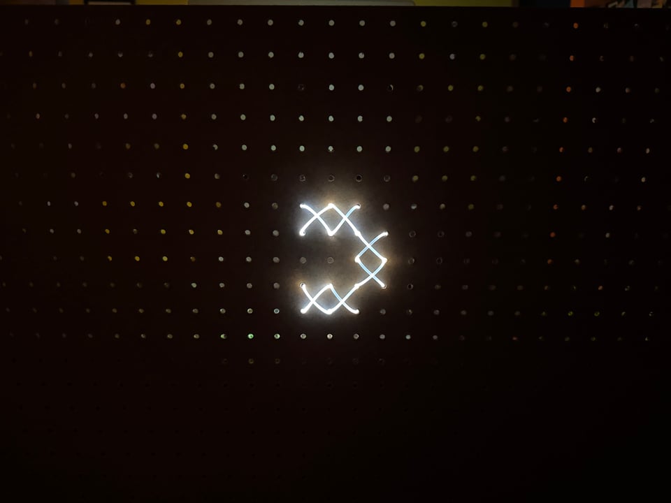 White illuminated cross-stitch on pegboard
