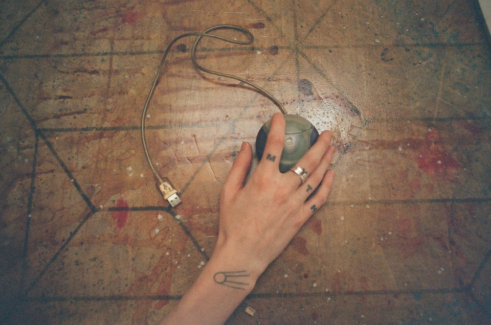 [A hand on an older Apple mouse. The surface that the mouse is on has some sort of diagram on it; it almost looks map-like.]