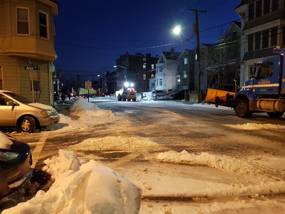 A photo of snow removal at night in an urban area of New Jersey.