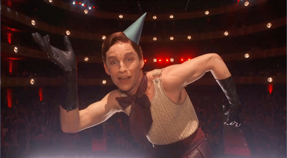 Eddie Redmayne in a party hat with his arms bent in the shape of a swastika