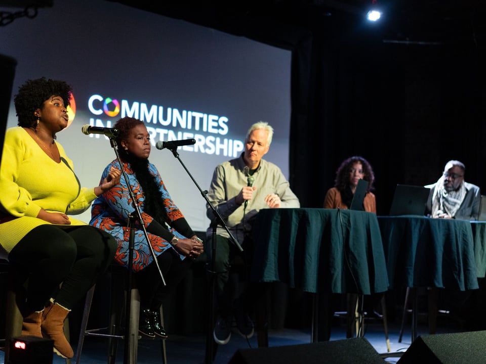 Image of event participants on stage in front of microphones