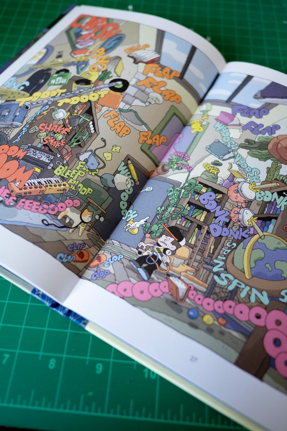 a spread from a comic. A kid and his cat are standing in a room, surrounded by flying objects and sound effects