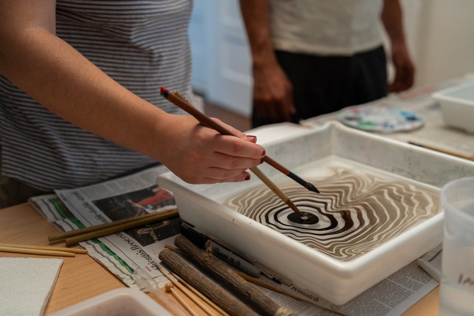 A person dips a brush into a bath of water and makes patterns.