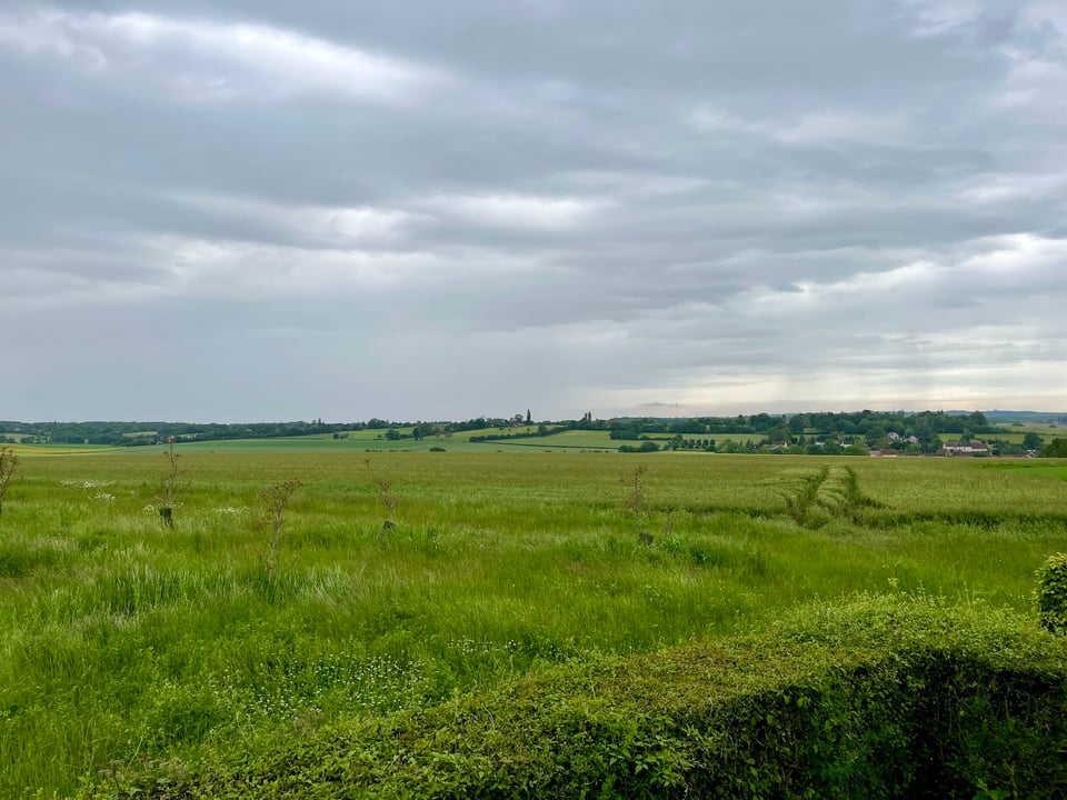 a grassy plateau with a village in distance to the right, grey clouds overhead