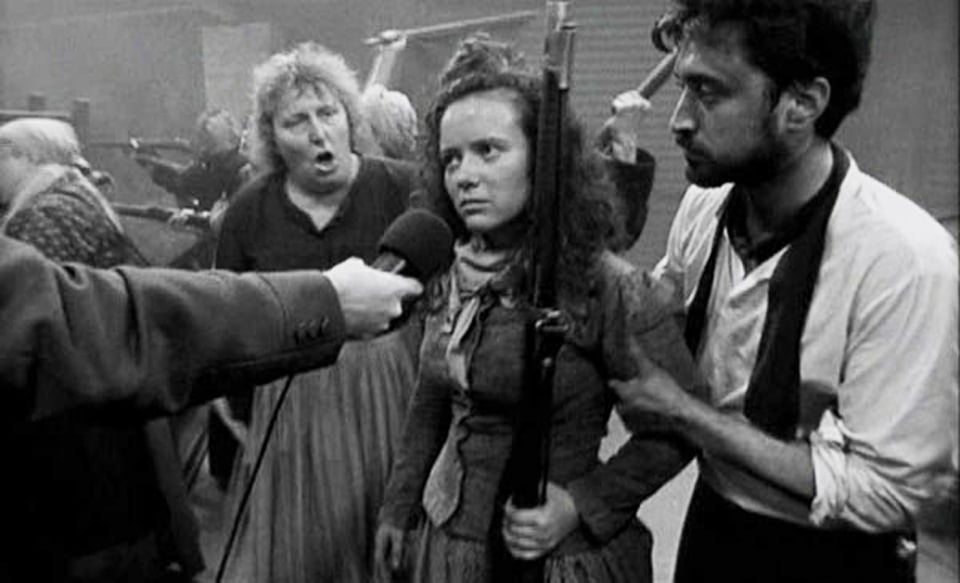 An angry young woman in period dress has a microphone thrust in front of her in La Commune