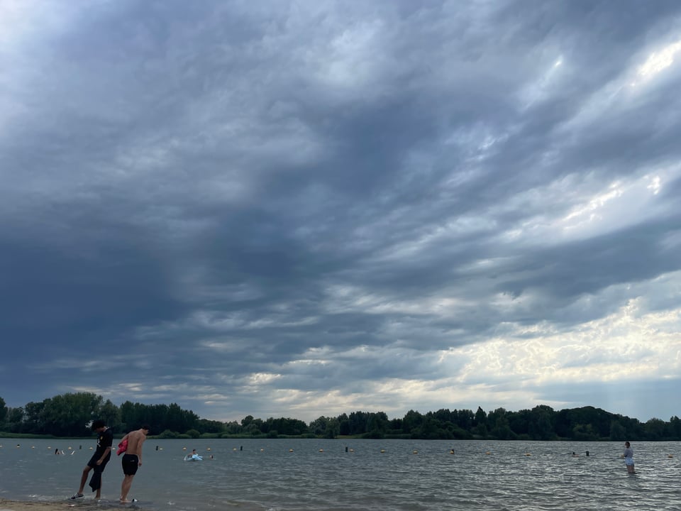 Storm clouds approaching over a lake with trees in the distance on the shore.