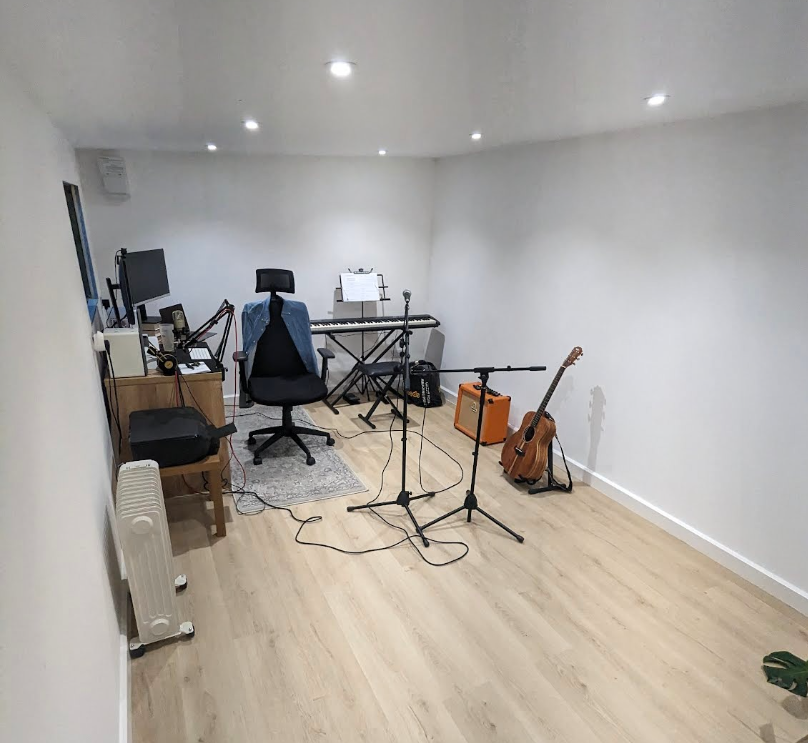 A home office with guitars, a desk, keyboard and mics