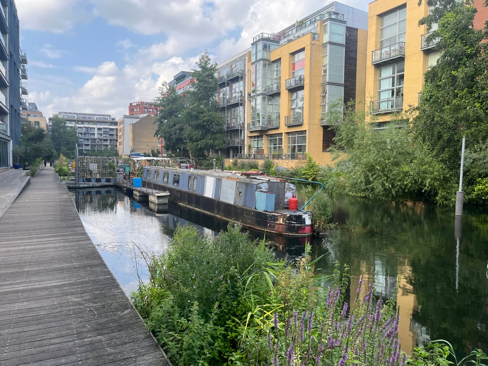 A more urban waterway, with tall residential buildings on all sides. There's still some greenery and plant life on the water's edge, and a riverboat sitting close to the bank.