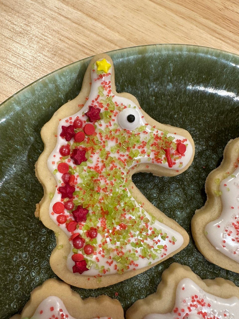 A unicorn head shaped cookie with a star on the horn, a big candy eye, green and red sugar sprinkle, and a mane of red sprinkles