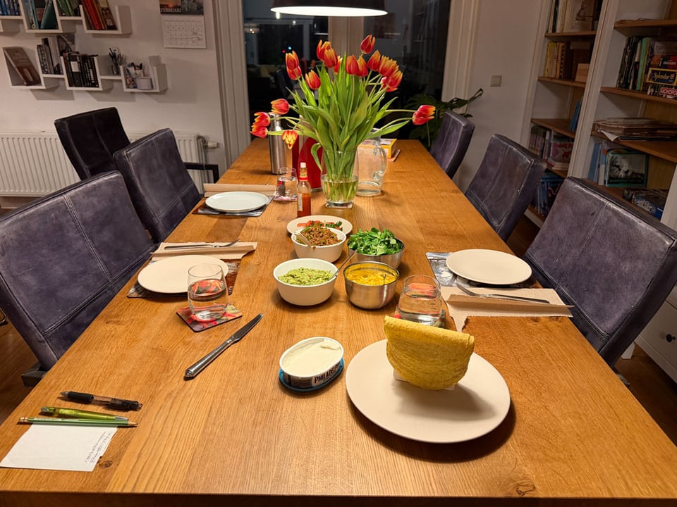 A dining room table is set for dinner. There are tacos ready to be made in the middle, there are plates and cutlery ready. There are orange and yellow tulips in the middle of the table.